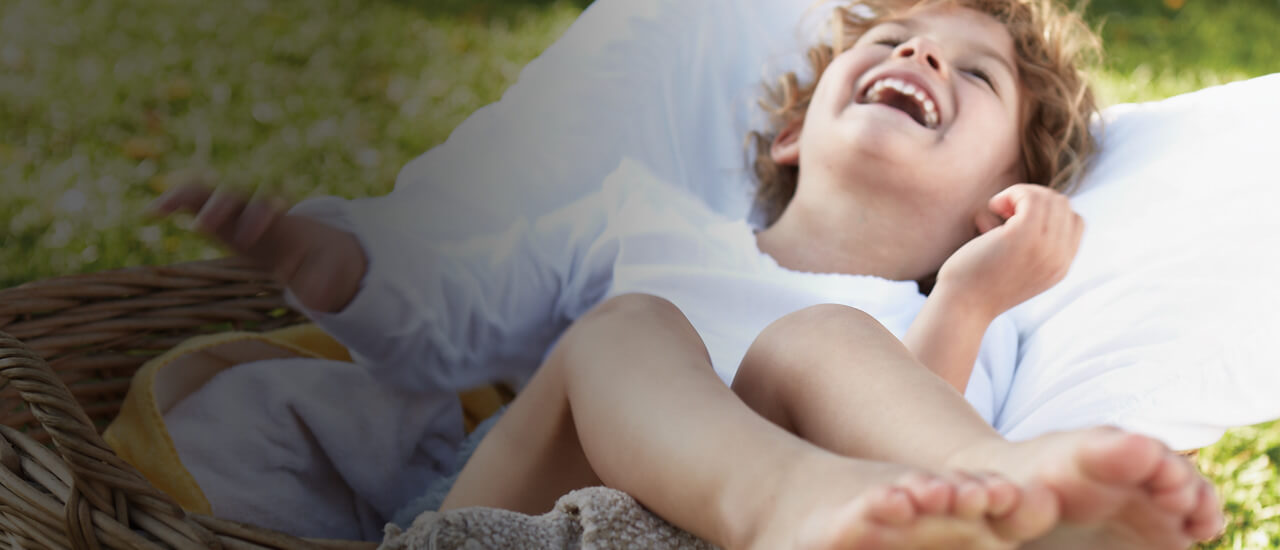 Imagen de una niña riendo sentada en una pila de ropa. Productos ecológicos para la limpieza del hogar y tus prendas.